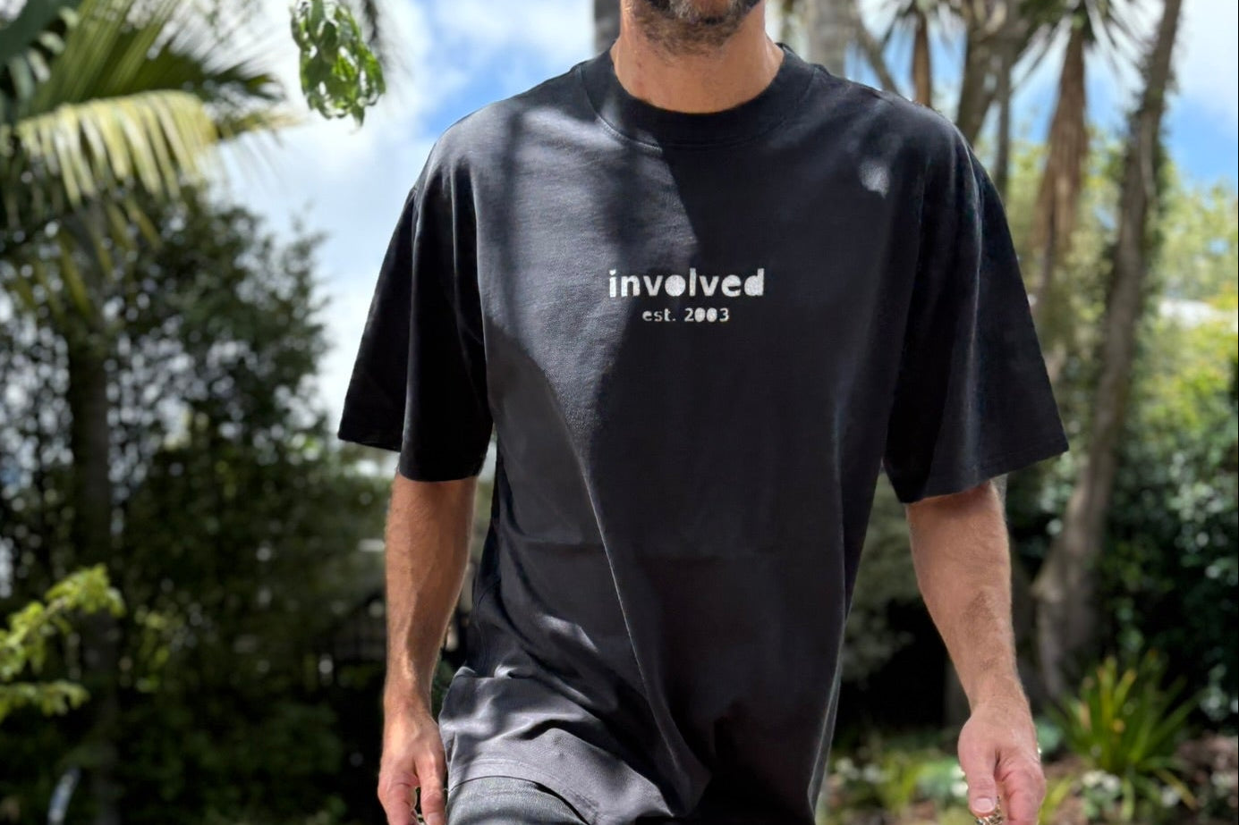 Man wearing a black t-shirt with 'involved' text, standing on a wooden deck
